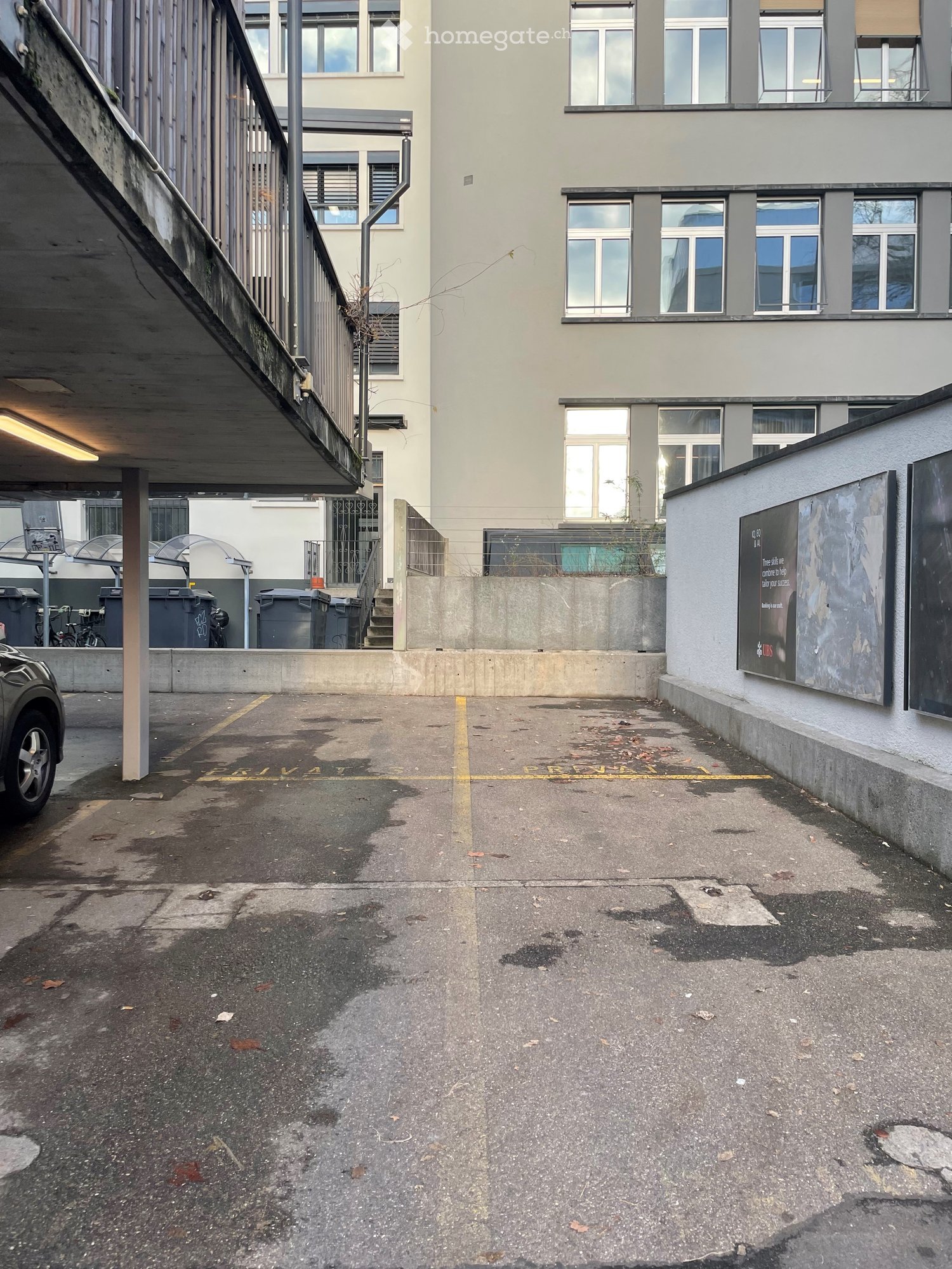 Empty parking lot in an apartment building with metal parking poles, concrete floor, and overhead lighting