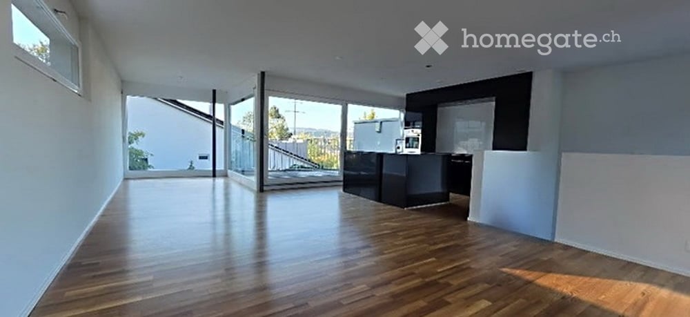 Open-plan space with wooden flooring, large windows, and a small black counter. No furniture or equipment visible.