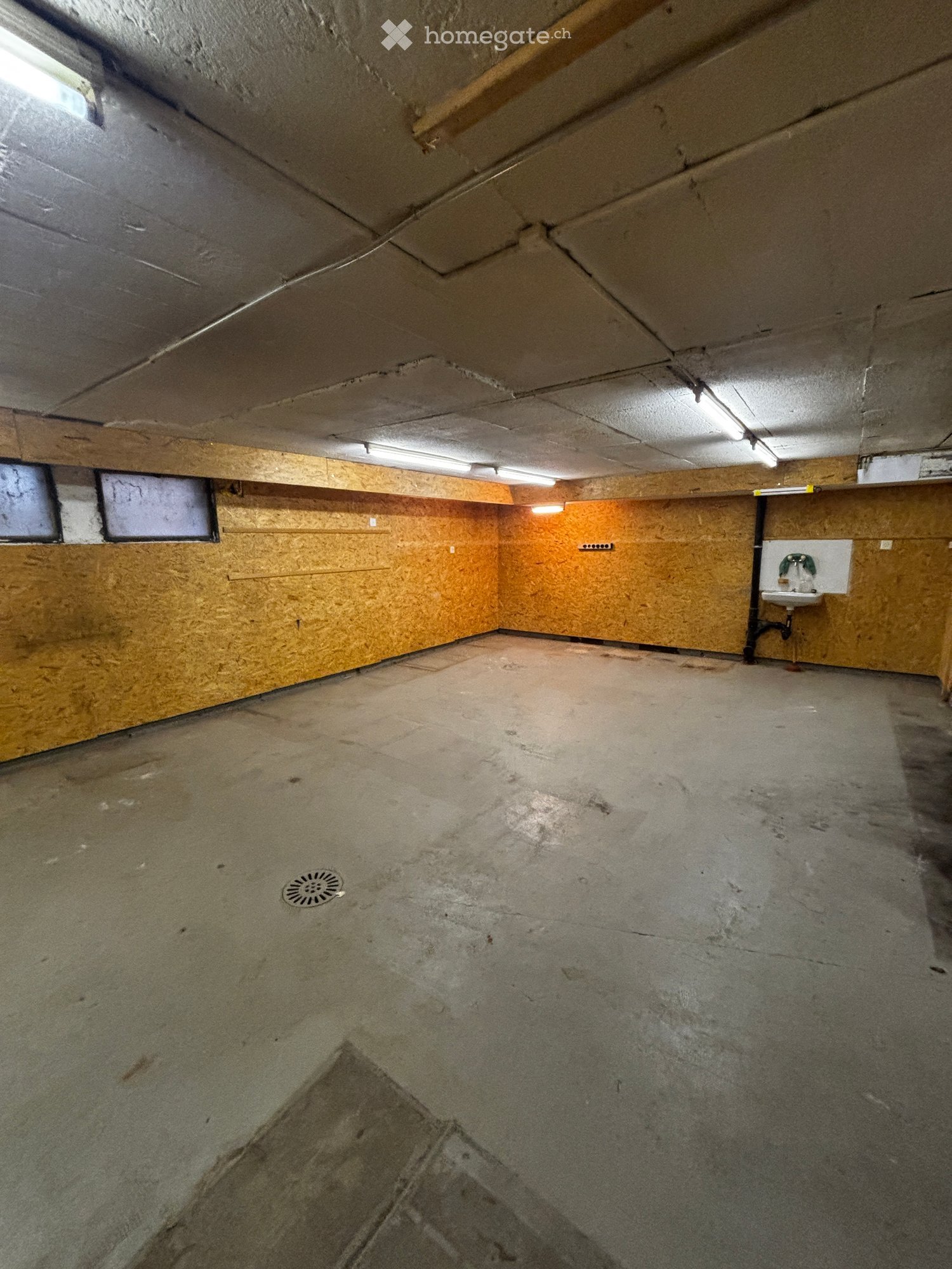 Empty basement space with concrete floor, exposed wooden beams, and a small sink in the corner.