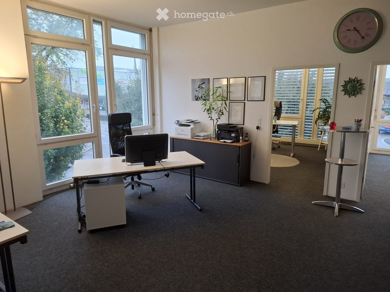 Office space with a desk, chair, computer, printer, small table, stool, clock, plant, and framed picture on the wall.
