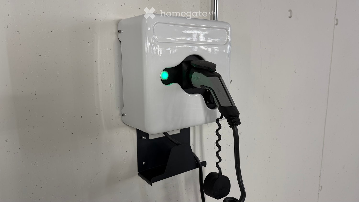 A white electric vehicle charging station mounted on a wall, with a green indicator light and a connected charging plug.