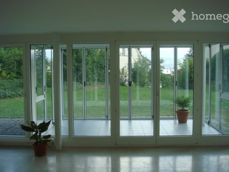 Bright, open room with large glass sliding doors leading to a patio, tiled floor, and two potted plants visible near the doors.