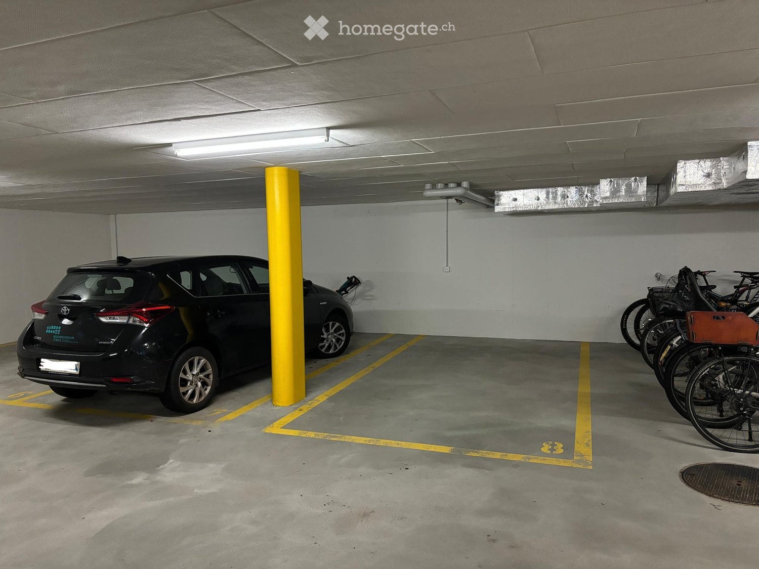 Underground parking area with a parked car and several bicycles, marked parking spaces, and a yellow support column.