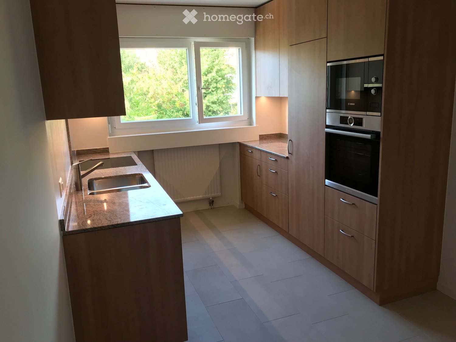 Modern kitchen with light wooden cabinets, stainless steel appliances, and a marble countertop.