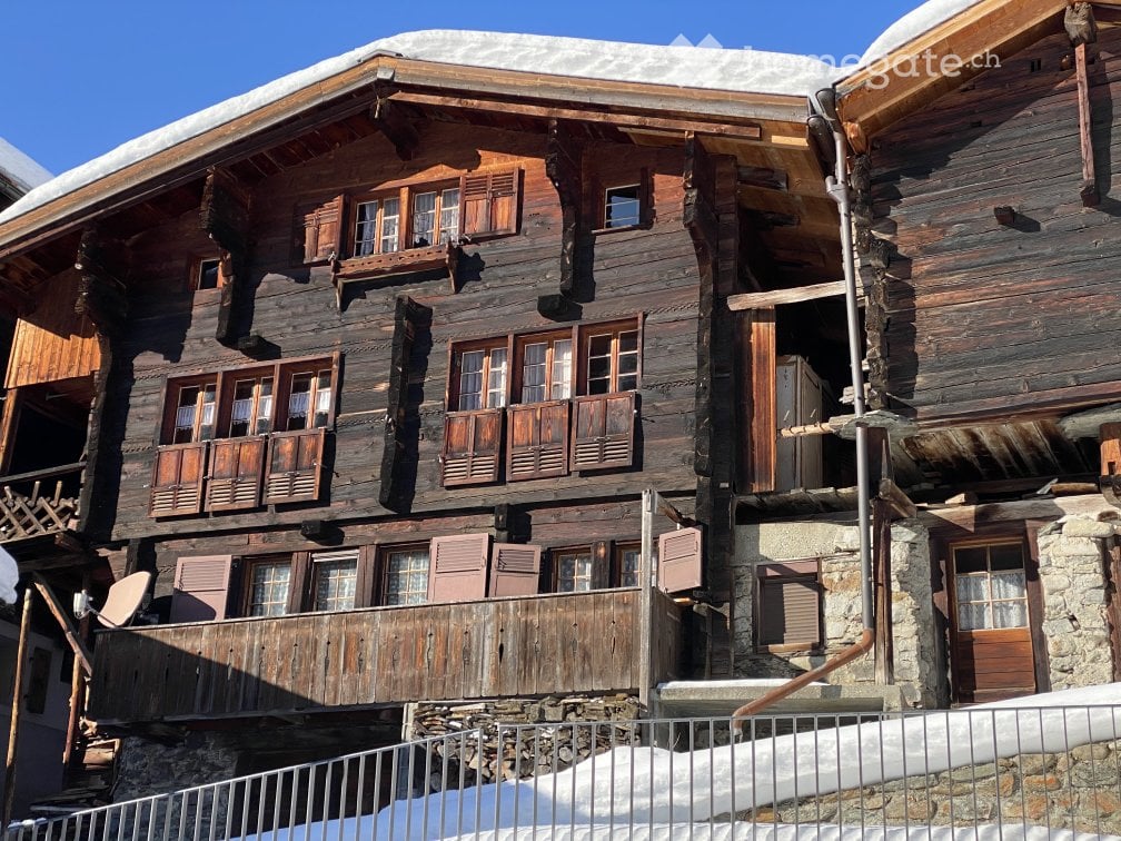 Traditional wooden chalet with multiple stories, wooden shutters, and stone base, surrounded by snow.