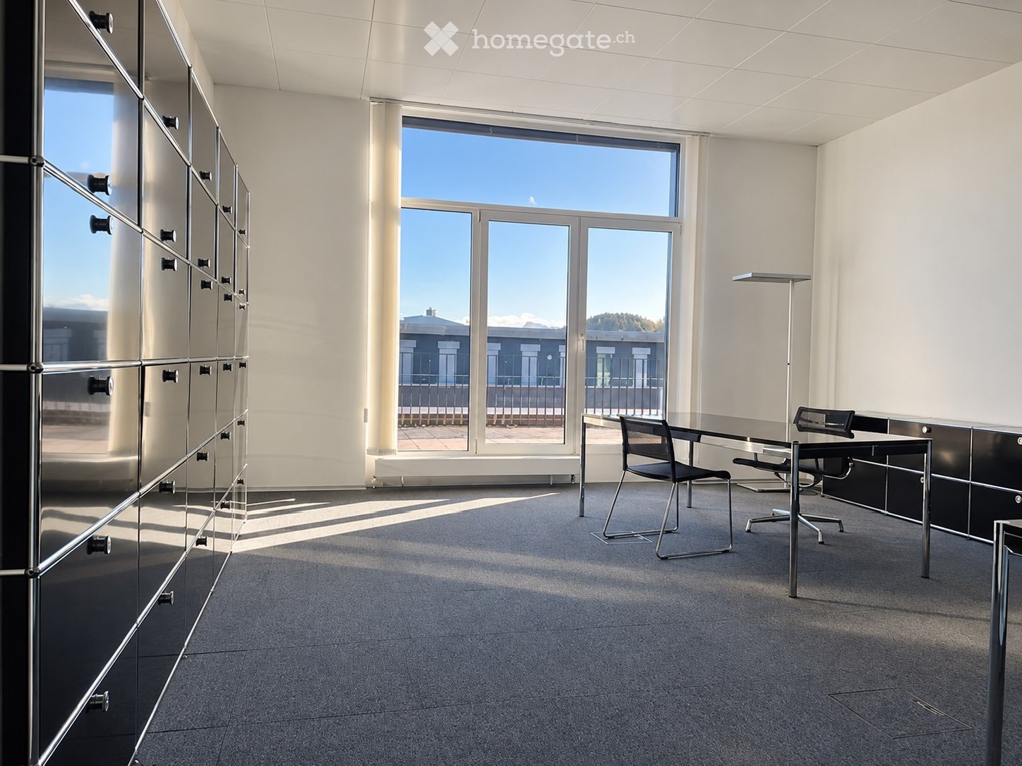 Modern, minimalist office space with large windows, glass partitions, and contemporary furniture including chairs, a table, and a cabinet.