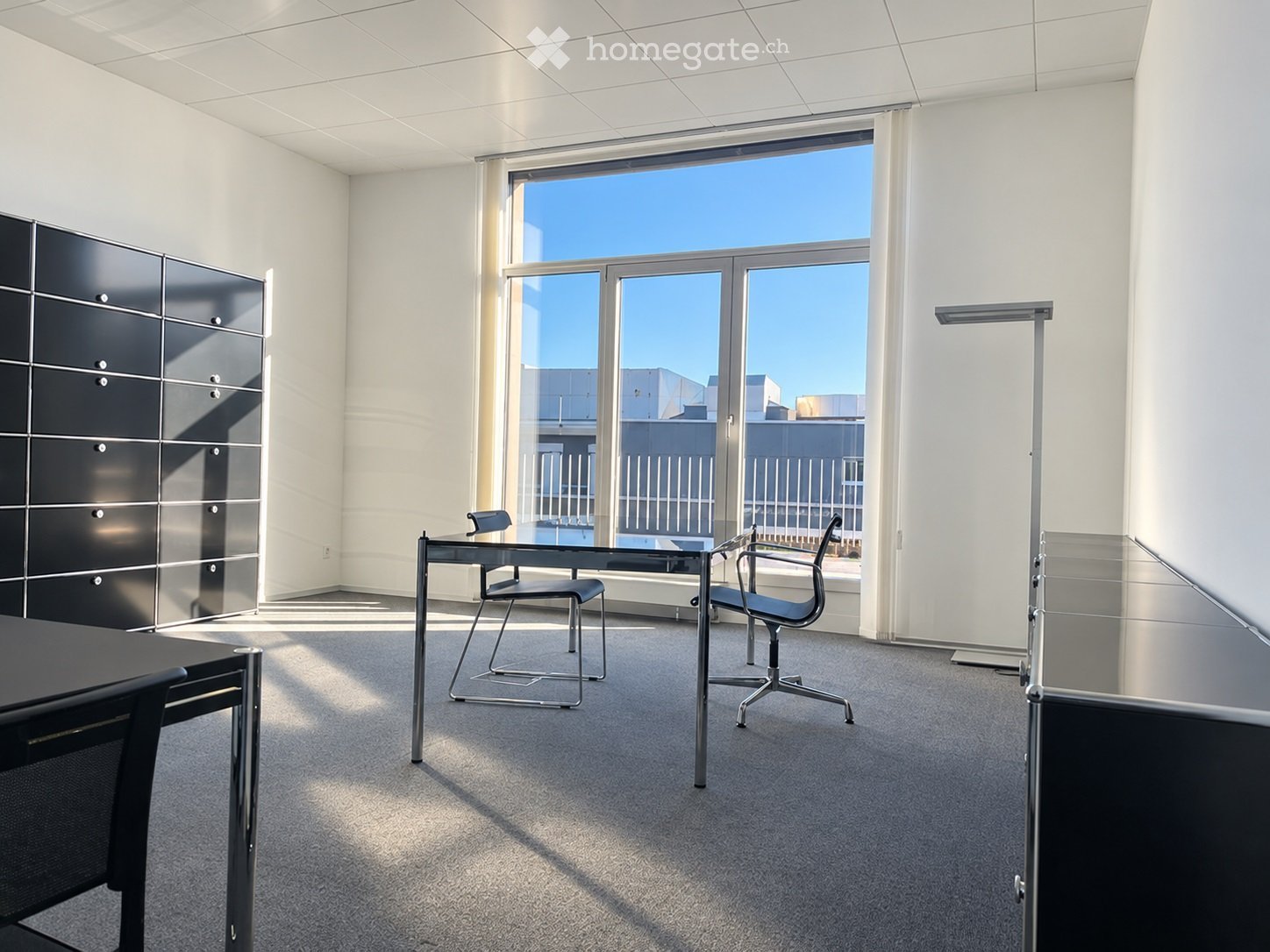 Modern office space with large windows, two chairs, a table, and a black cabinet.