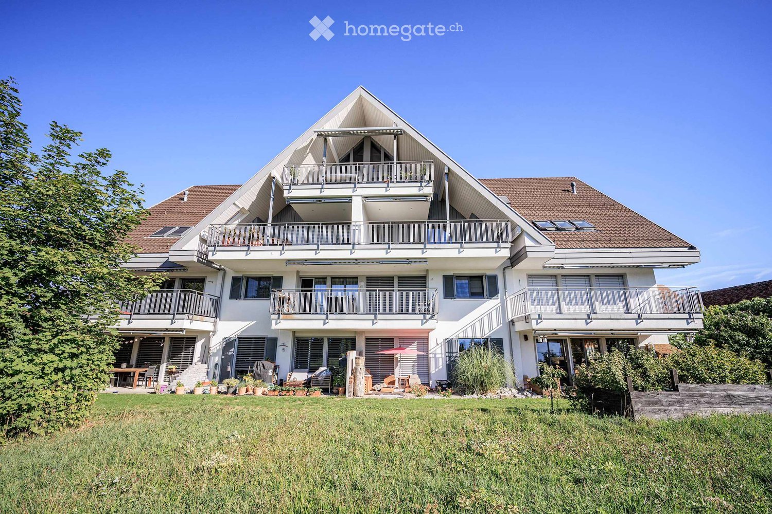A modern two-story house with white exterior, multiple balconies, and a well-maintained lawn in front.