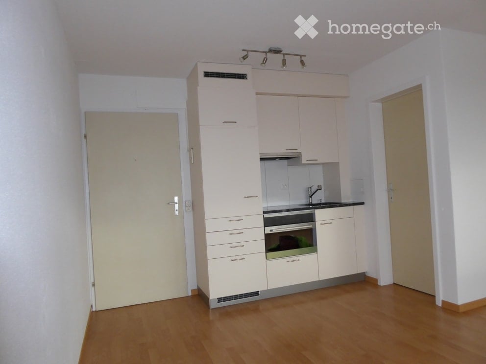 Modern kitchen with light-colored cabinets, an oven, and a faucet, featuring wooden flooring and white walls.