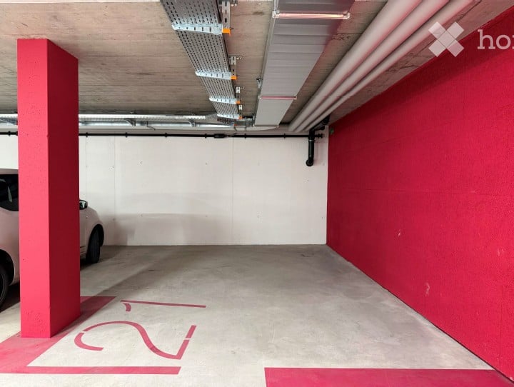 Underground parking area with a single car parked, marked parking spaces, and structural pillars.