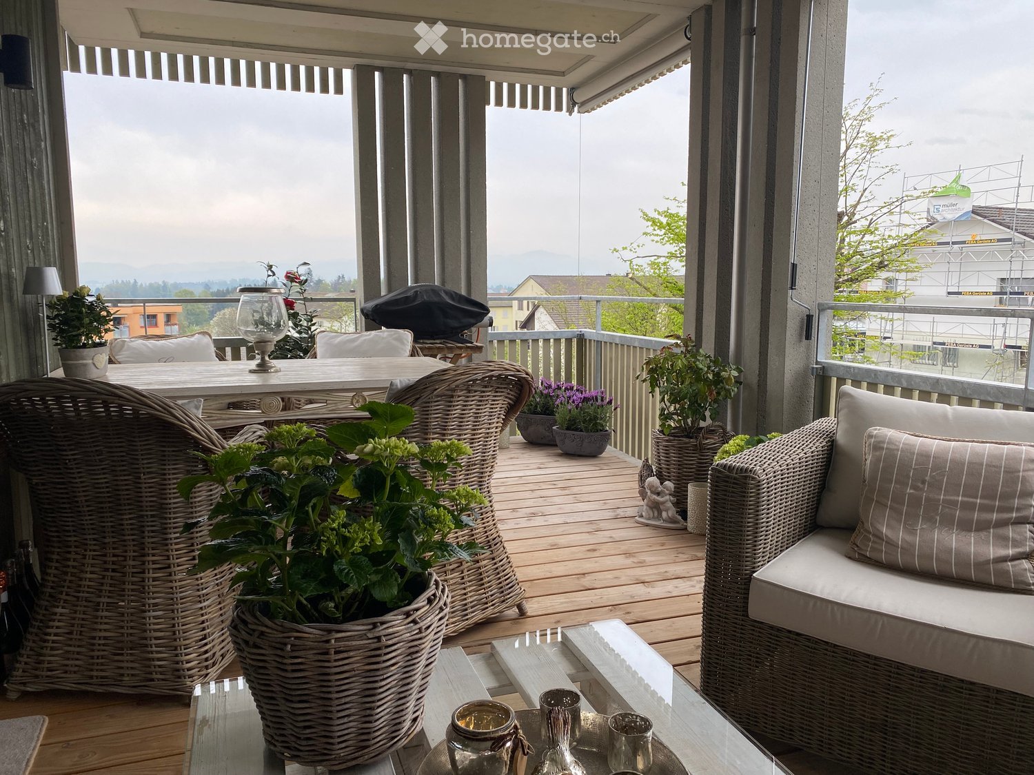 Balcony with wicker furniture, glass table, potted plants, and decorative items.