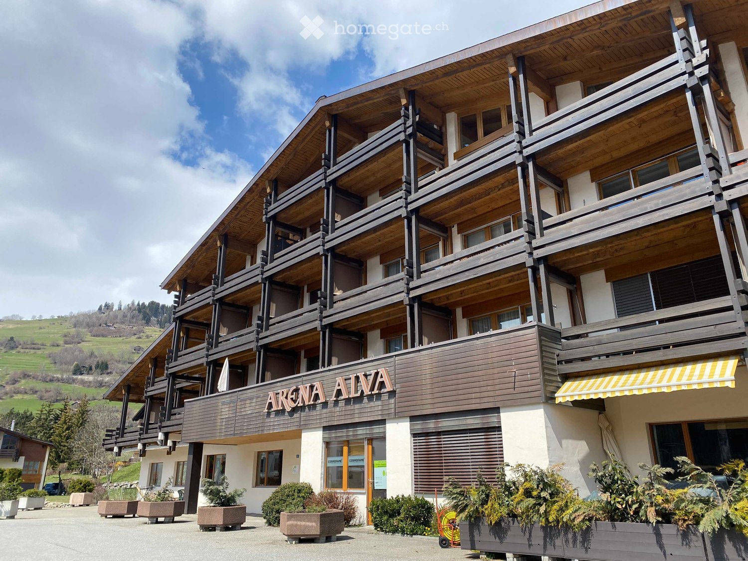 Modern building with wooden exterior, multiple floors with balconies, a yellow awning