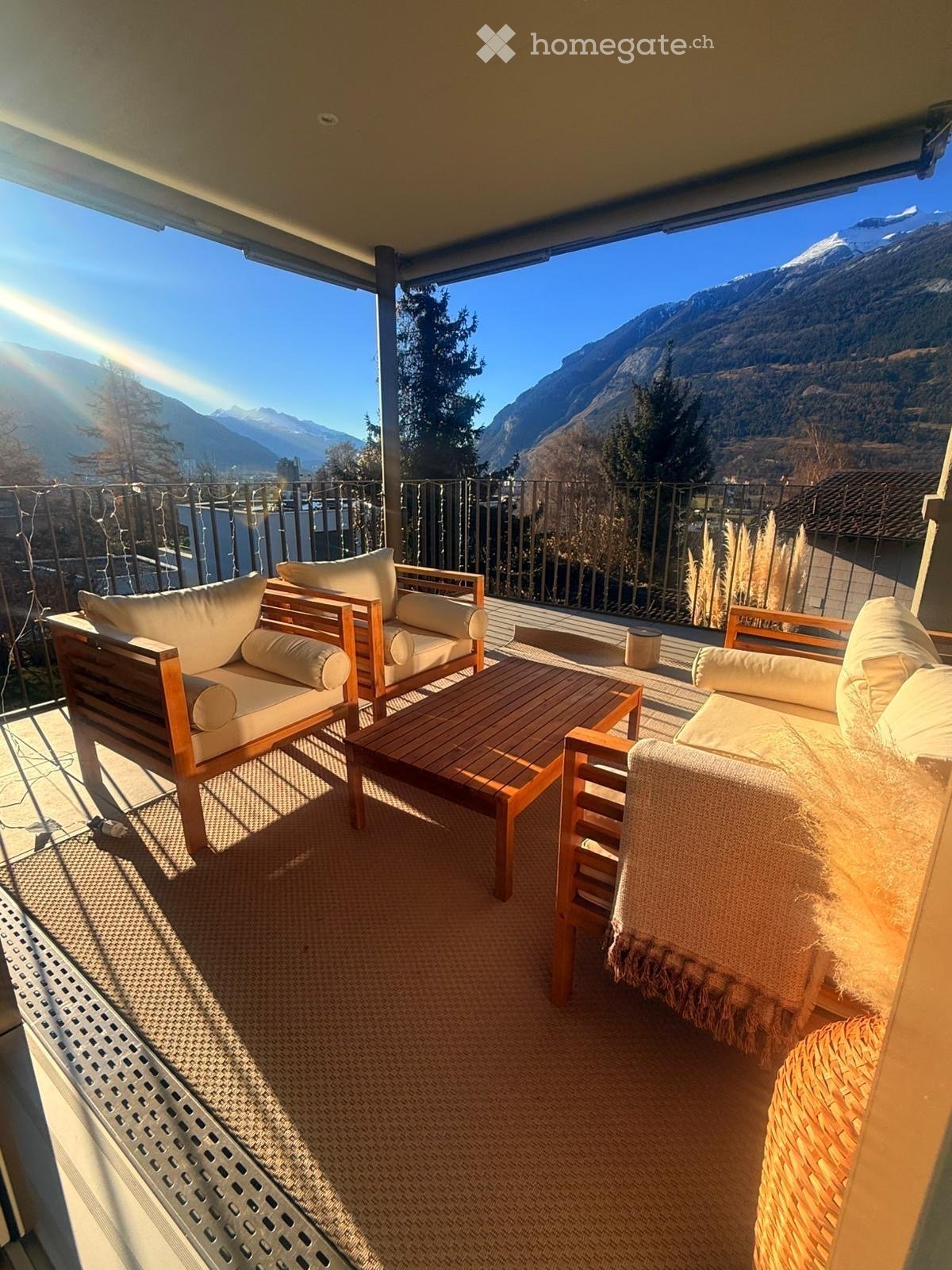Balcony with wooden furniture, including a sofa, table, and chairs, overlooking a mountain view.