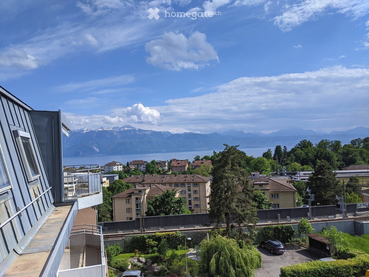 Balcony overlooking a suburban area with houses, trees, and a distant lake and mountain range.