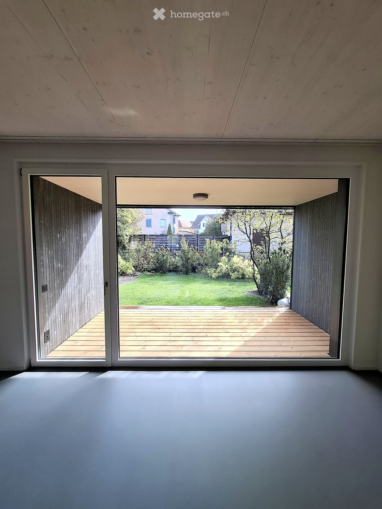 Empty room with large sliding glass doors leading to a wooden deck and a green garden area.