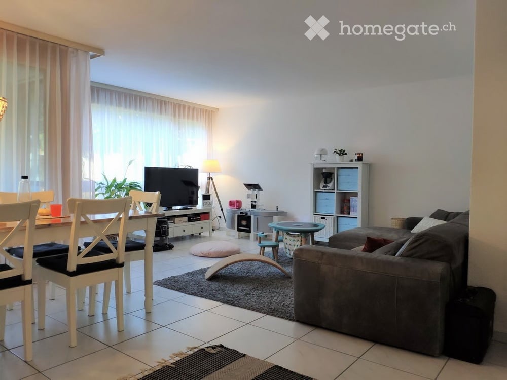 A modern living room with a grey sofa, coffee table, dining table with chairs, television, floor lamp, small round table, and decorative items.