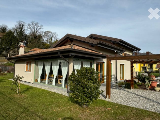 Single-story house with a tiled roof, large windows, and a covered outdoor patio area with furniture.