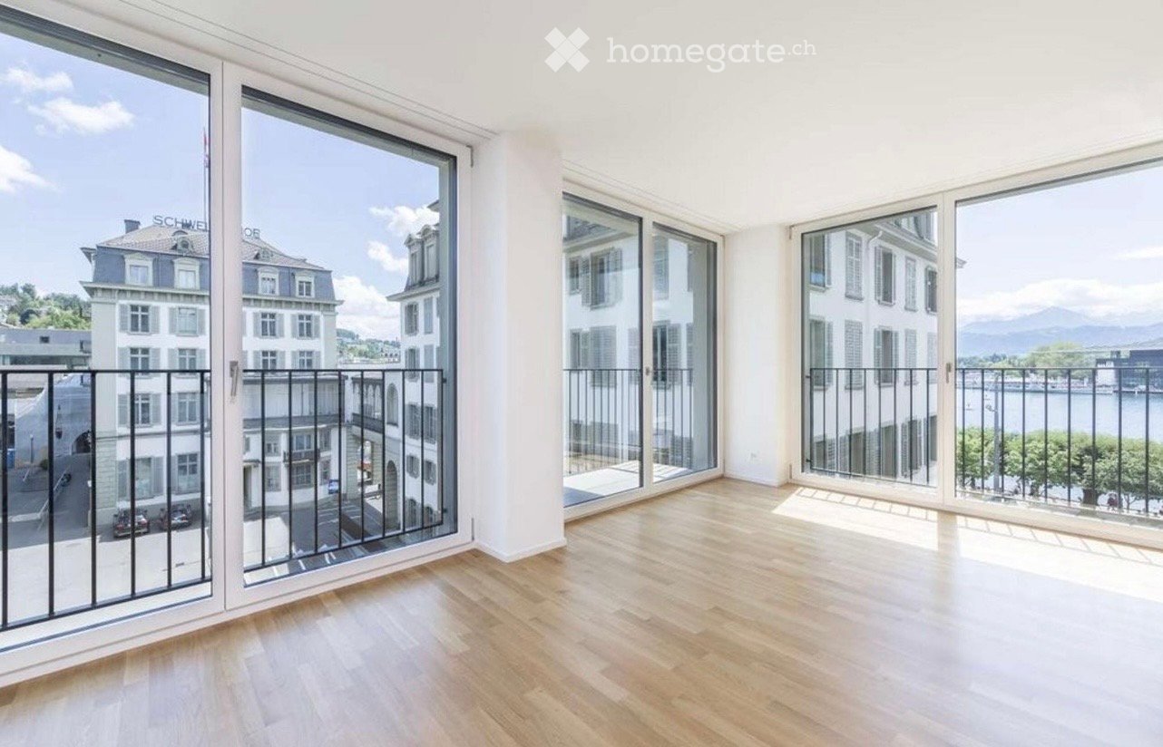 Bright, empty room with large windows and wooden flooring, offering a scenic view of the city and mountains.