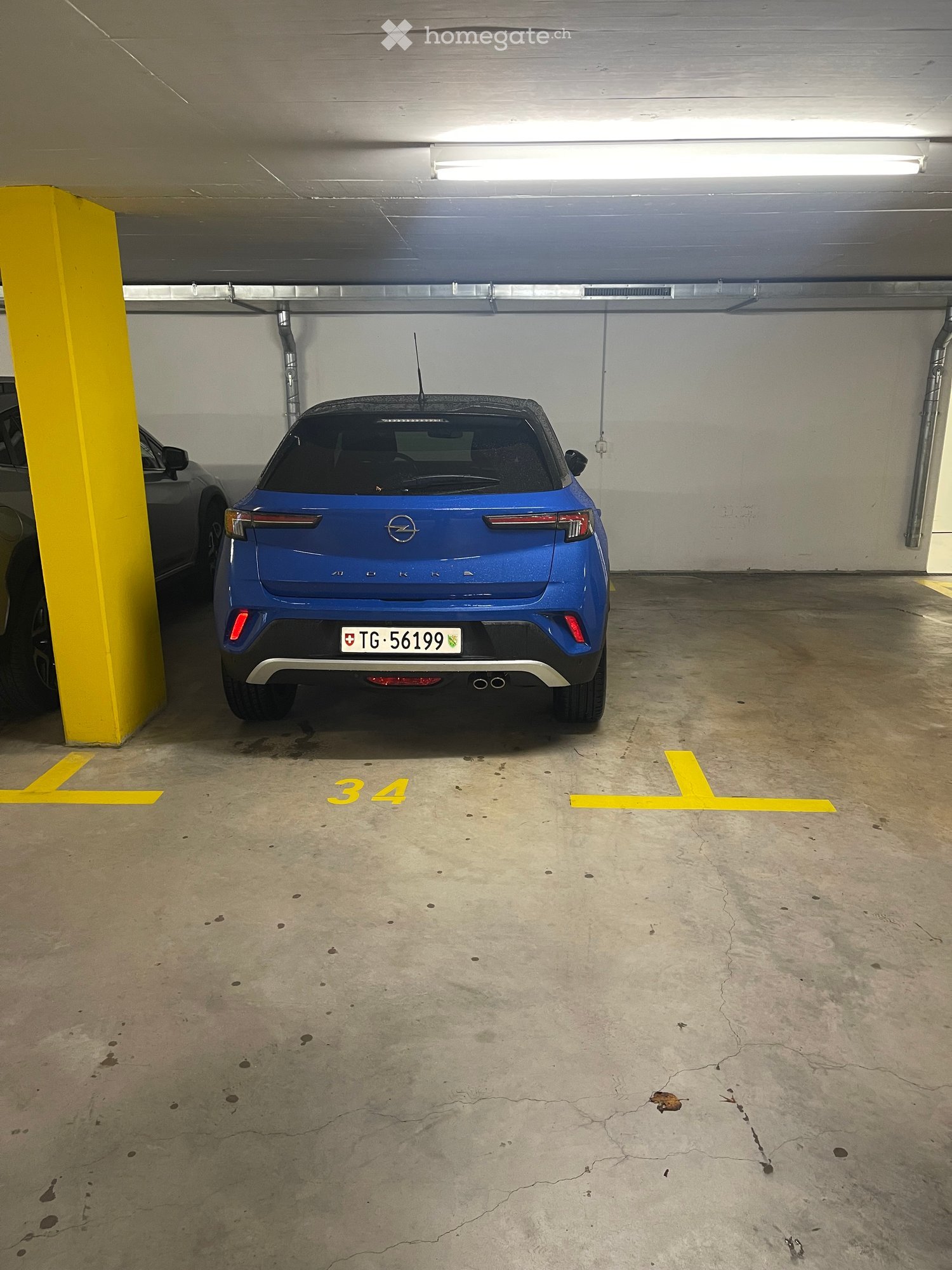 Underground parking area with a blue car parked in bay number 34, marked with yellow lines and a yellow pillar.