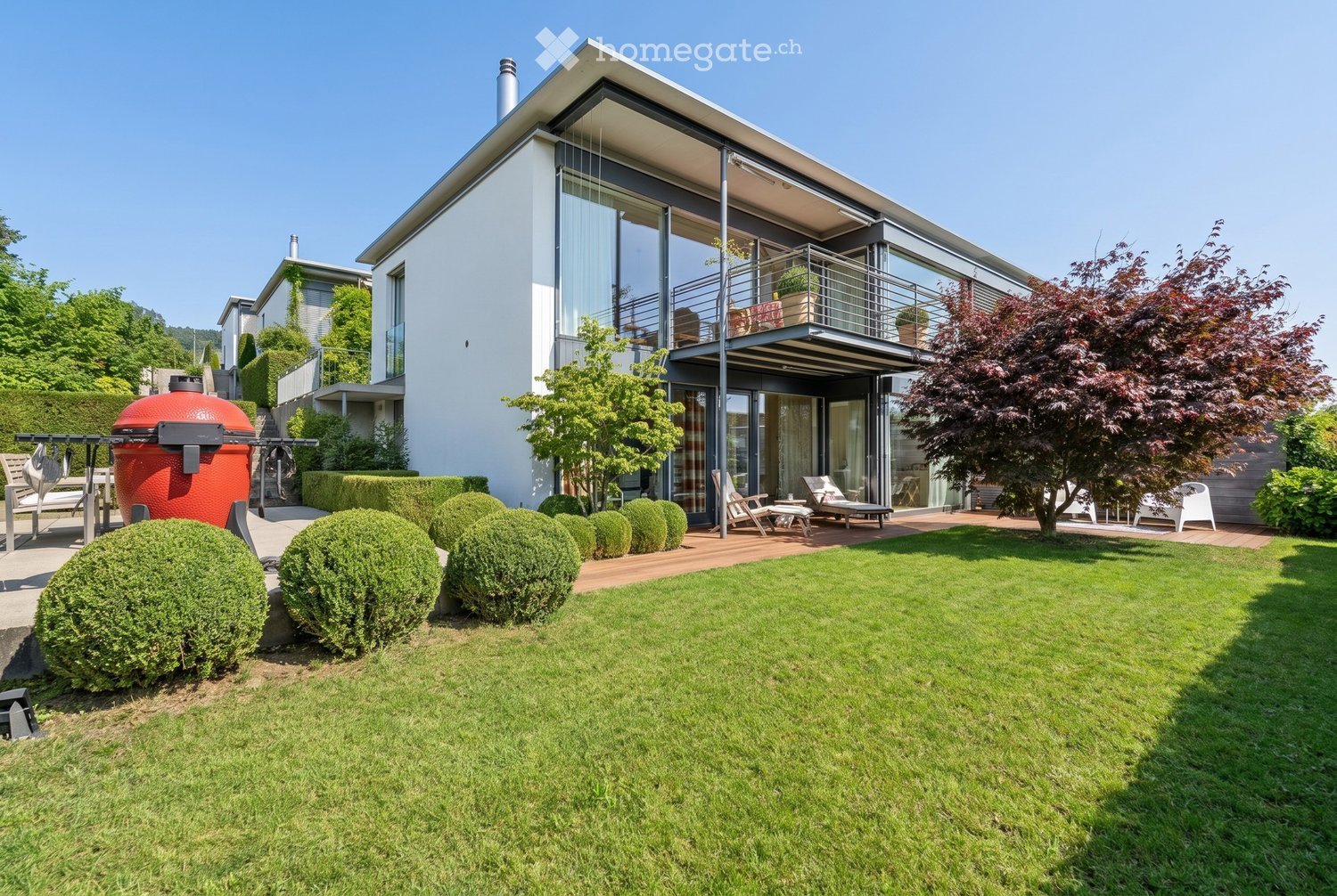 Modern house with a spacious garden, featuring a well-maintained lawn, neatly trimmed hedges, outdoor seating, and a large barbecue grill.