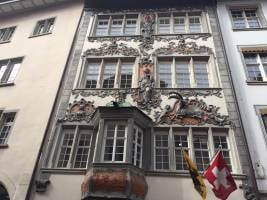 Ornate historic building facade with intricate carvings, multiple windows, and flags displayed on the side.