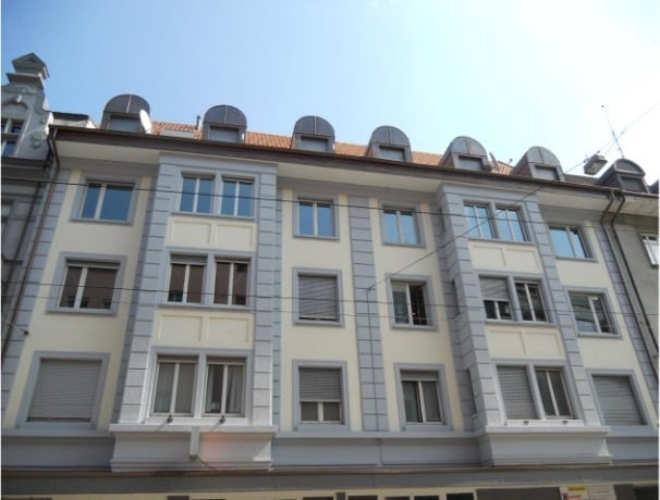 Multi-story residential building with light-colored facade, multiple windows, and decorative roofline.