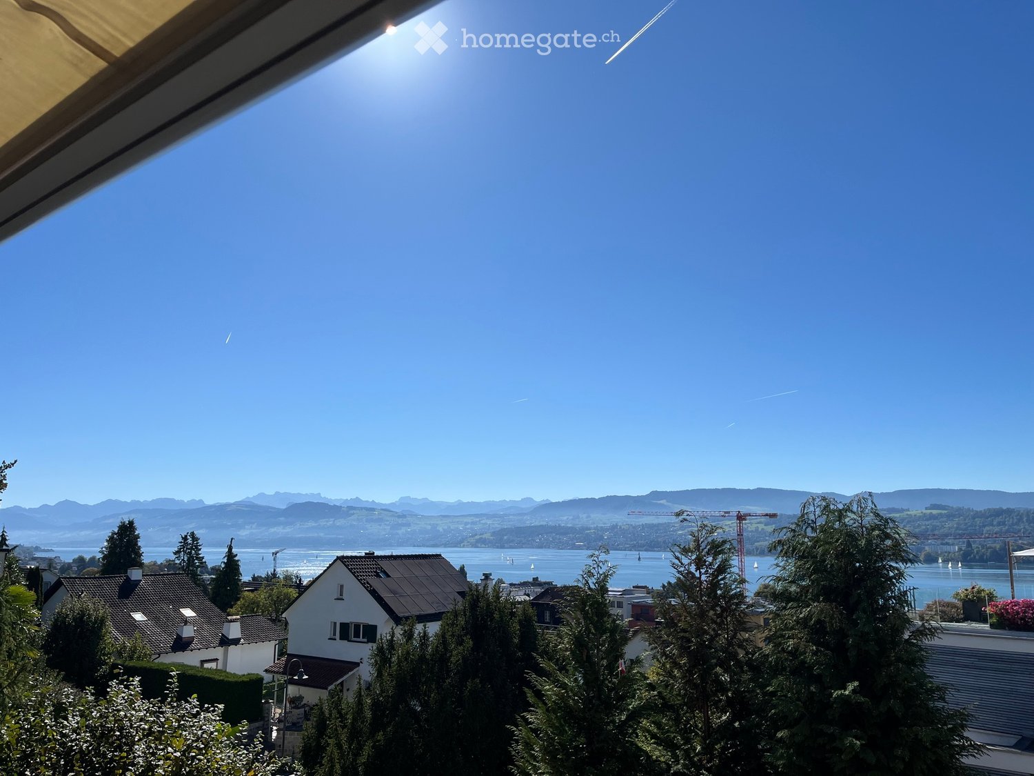 View from a window showing a scenic landscape with a lake, mountains, houses, and trees.