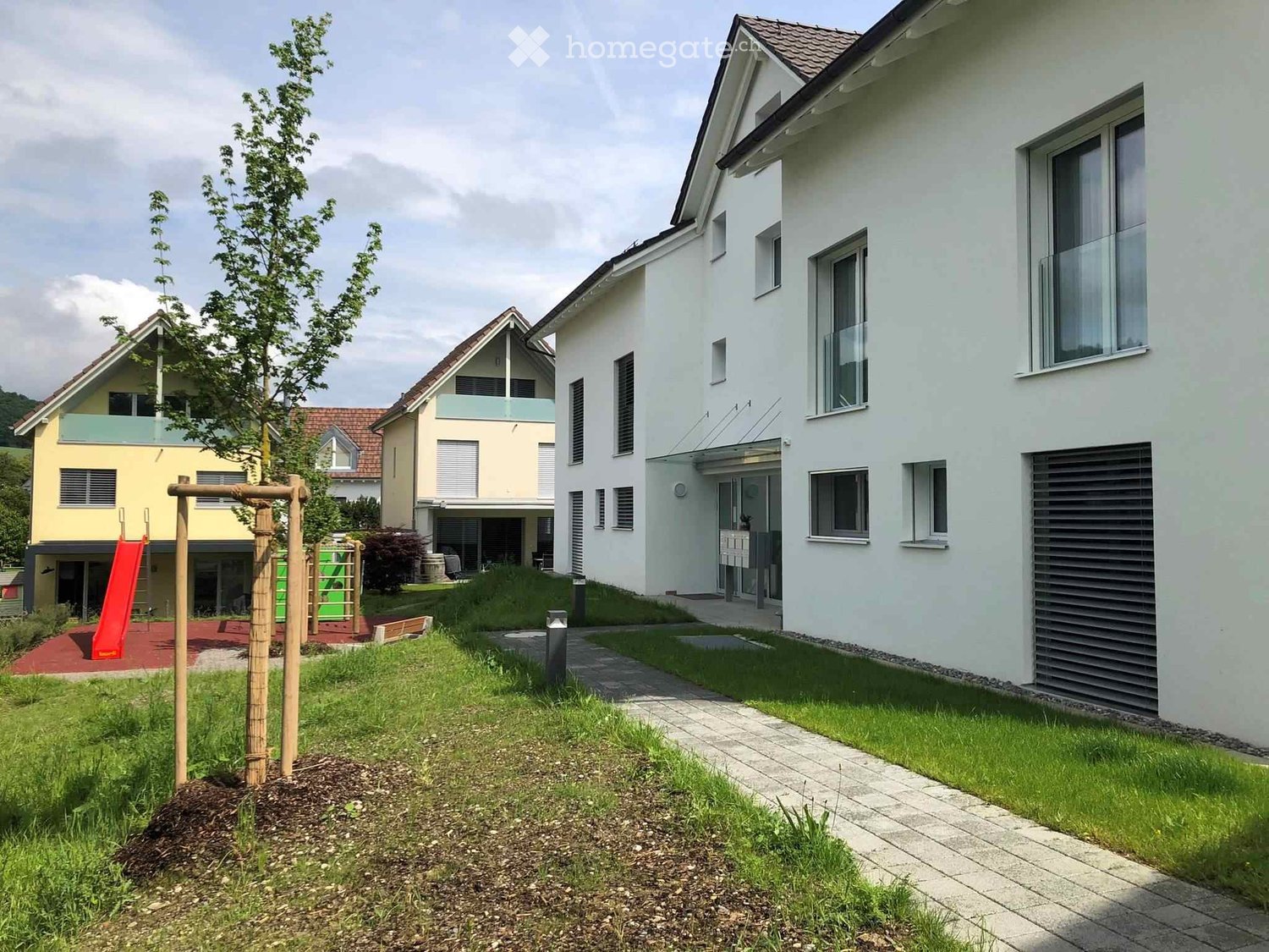 Residential area with modern houses, a playground with a slide, and a paved pathway.