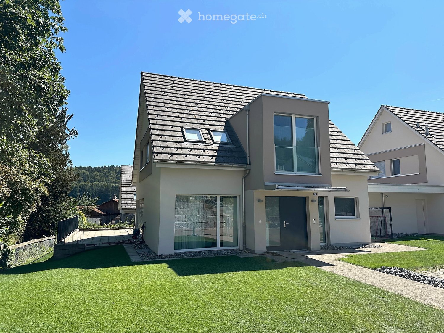 Modern two-story house with a gray roof, large windows, and a well-maintained lawn in front.