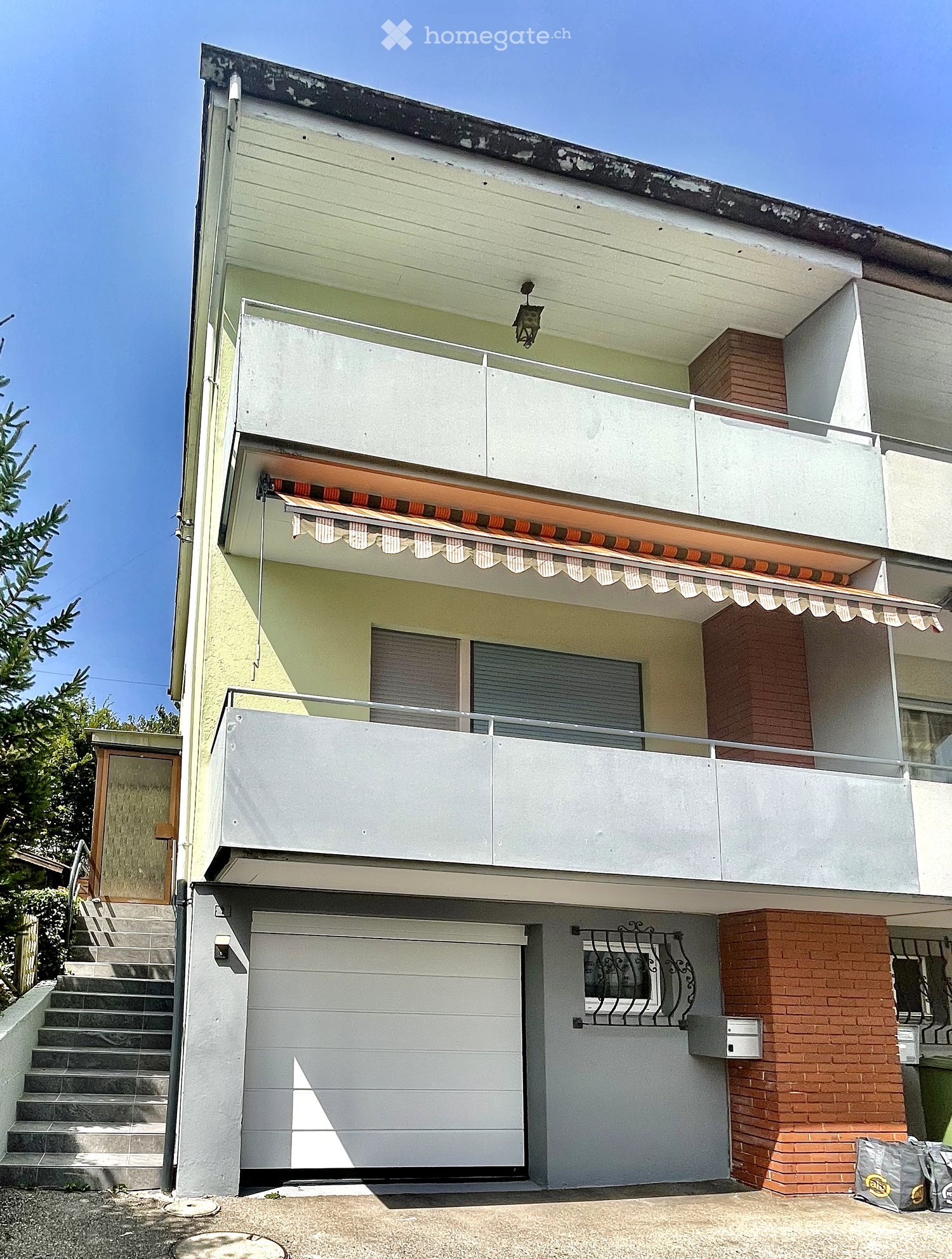 Two-story house with white and light green exterior, garage, balcony, and covered entrance with awning.