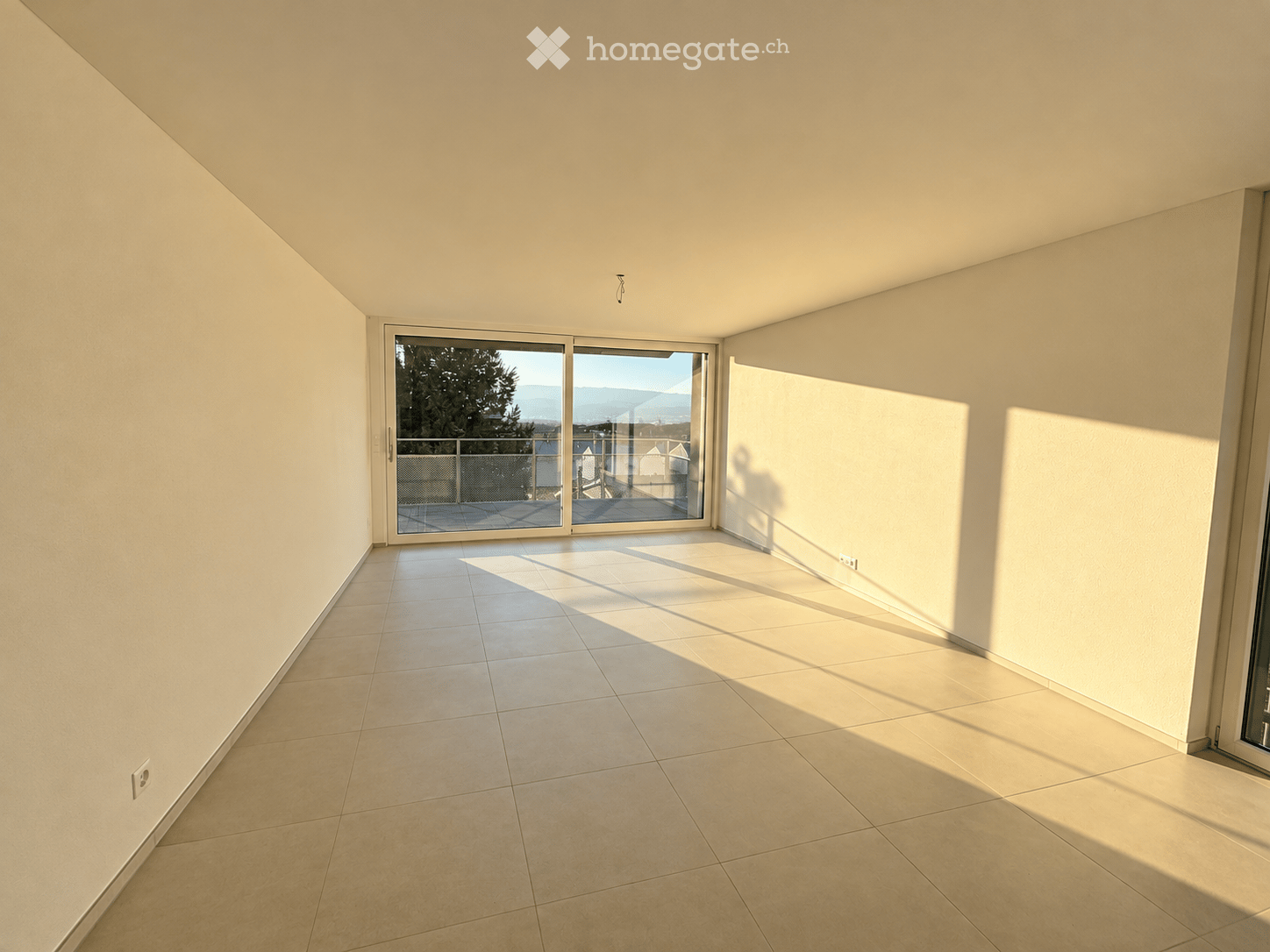 Empty room with tiled floor, large sliding glass door leading to a balcony, and natural light streaming in.