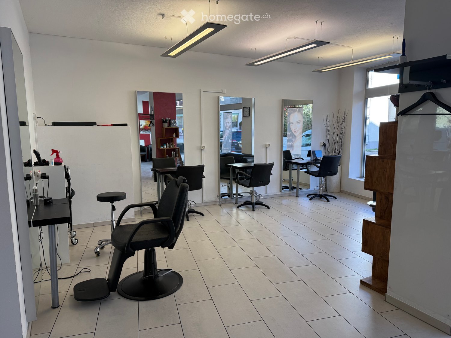 Modern salon with tiled floor, multiple black salon chairs, mirrors, and a small table with a spray bottle and other items.