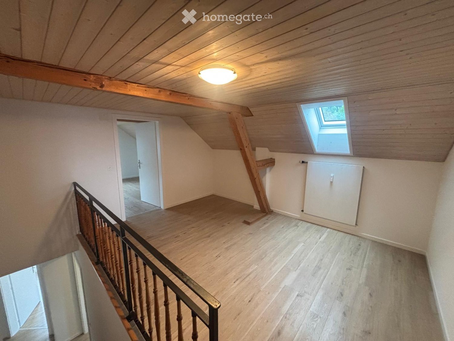 Spacious attic hallway with wooden floors, exposed wooden beams, a skylight window, and a staircase leading downwards.