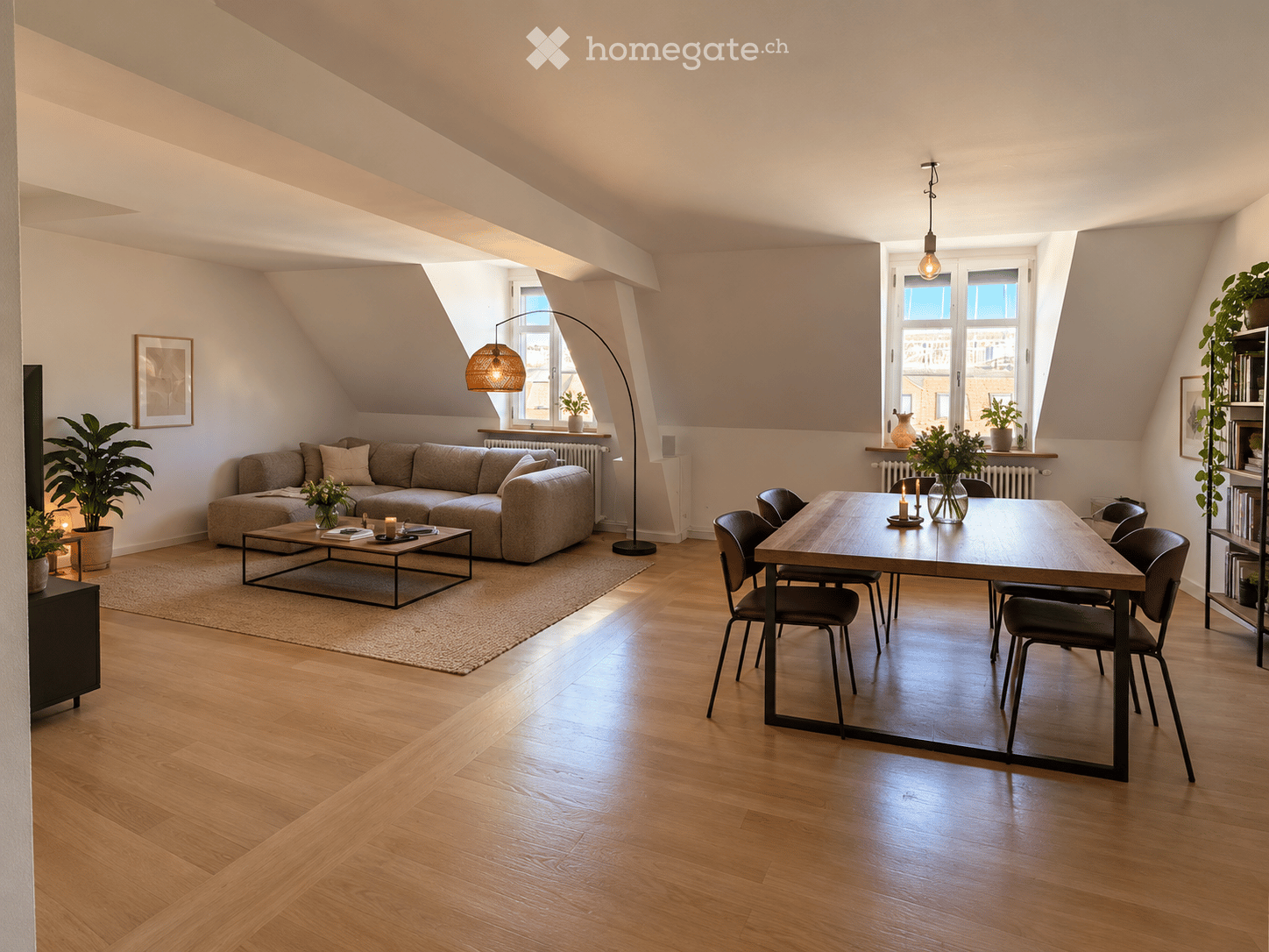 Modern living and dining area with wooden flooring, a grey sectional sofa, a coffee table, a dining table with chairs, floor lamp, and decorative plants.