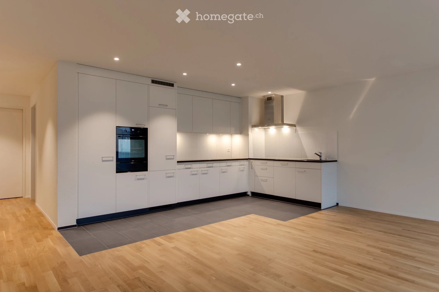 Modern kitchen with white cabinets, wooden flooring, and built-in appliances including an oven and range hood.