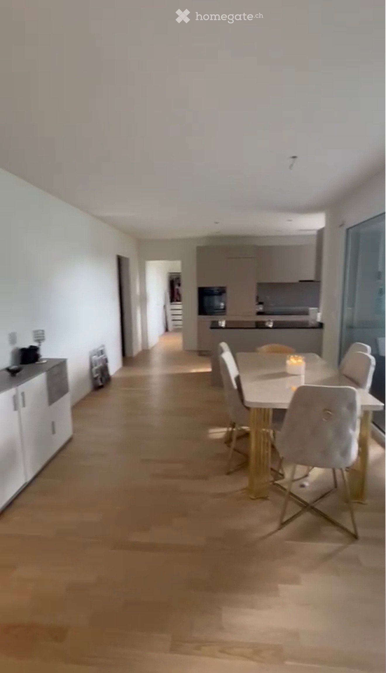 Modern dining area with a white dining table, four chairs, and a microwave in the adjacent kitchen area.