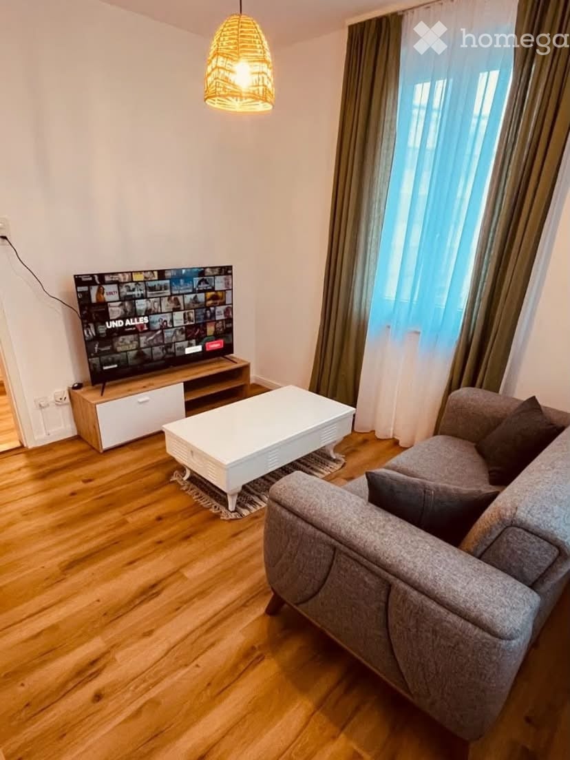 Modern living room with wooden flooring, grey sofa, white coffee table, television, and a hanging lamp.