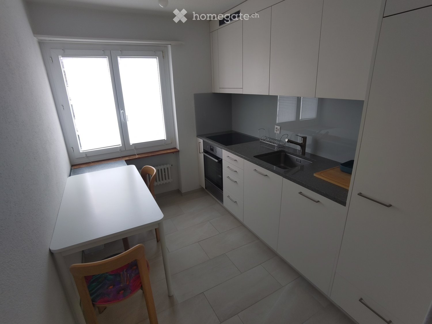 Modern kitchen with white cabinets, dark countertops, a sink, oven, and a small dining area with a table and chairs.