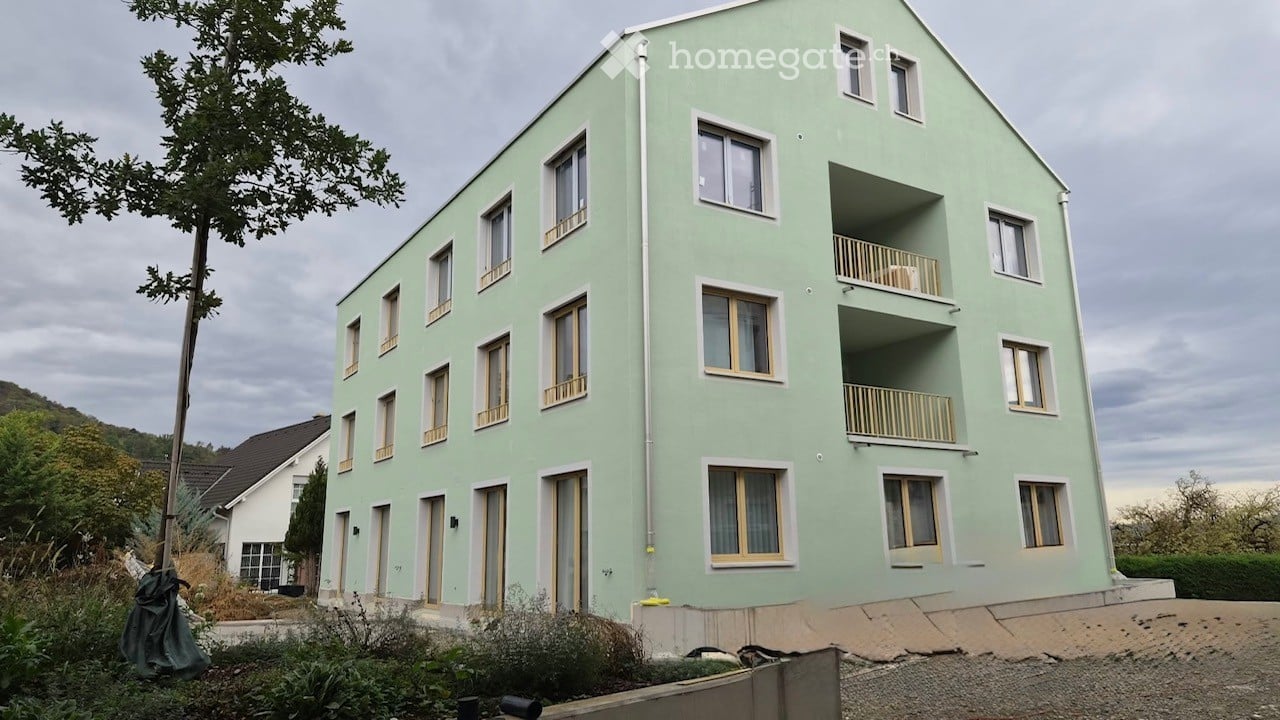 Modern two-story building with light green exterior, multiple windows, and balconies on the upper floor.