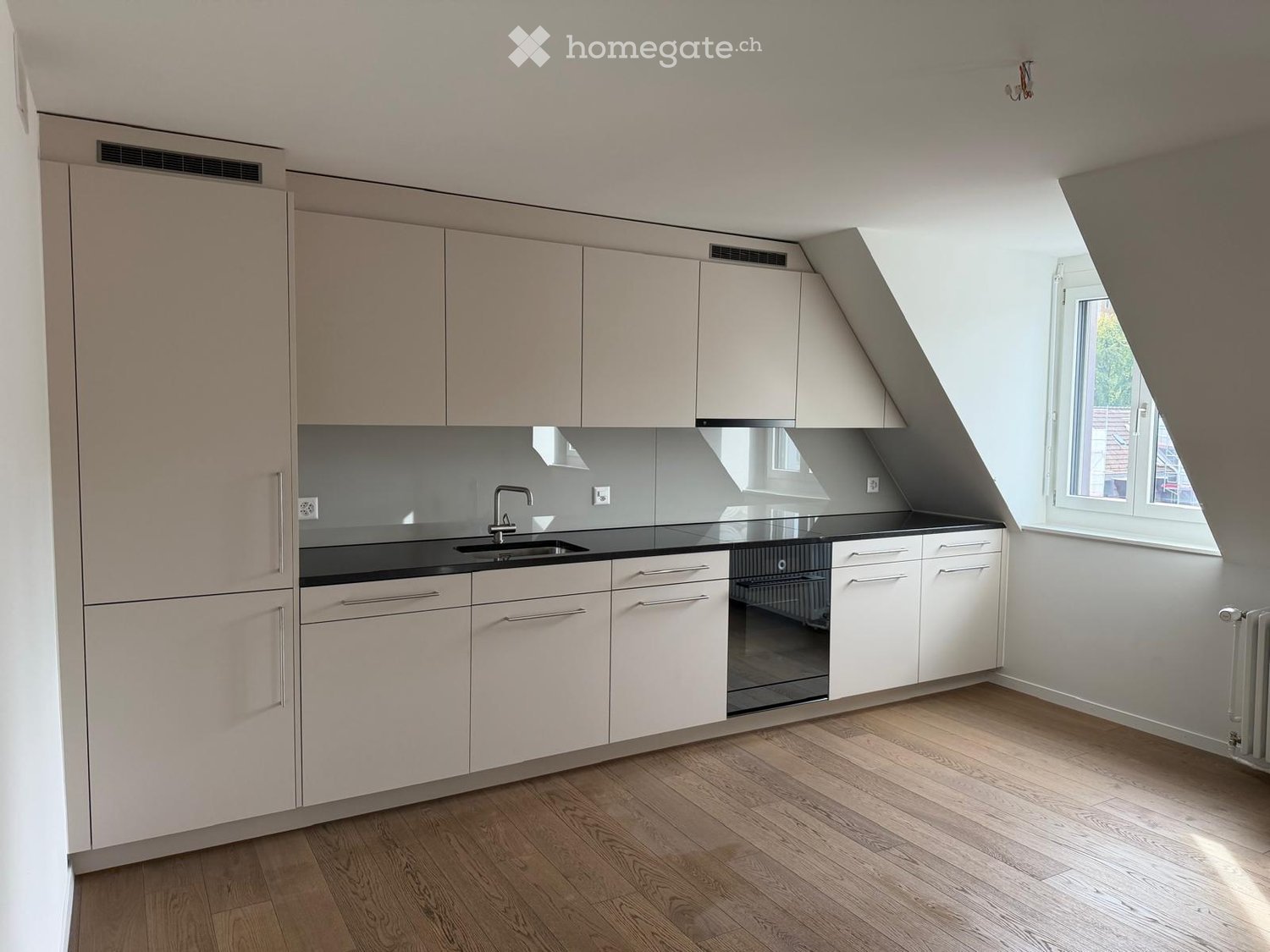 Modern kitchen with white cabinets, black countertops, and a stainless steel sink. The space features wooden flooring and a large window allowing natural light to enter.