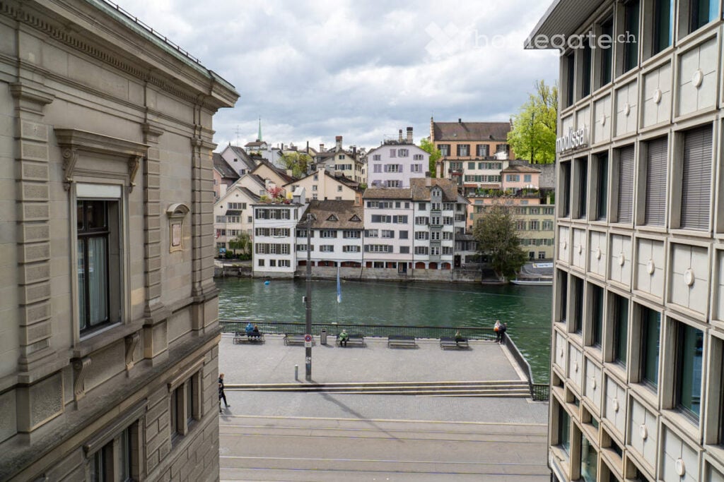 View of a cityscape with historic buildings, a river, and a waterfront promenade.