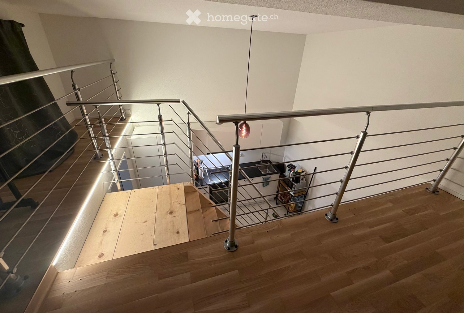 Modern staircase with wooden steps and metal railing, leading to a kitchen area visible below.