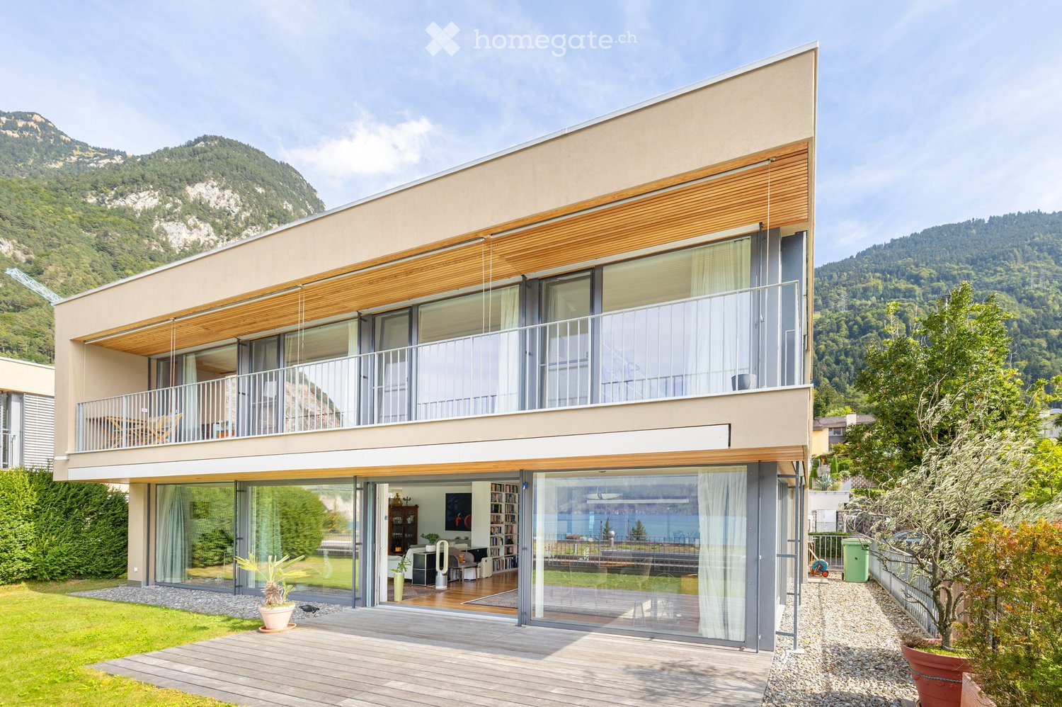 Modern two-story house with large windows, wooden accents, and a scenic mountain view in the background.