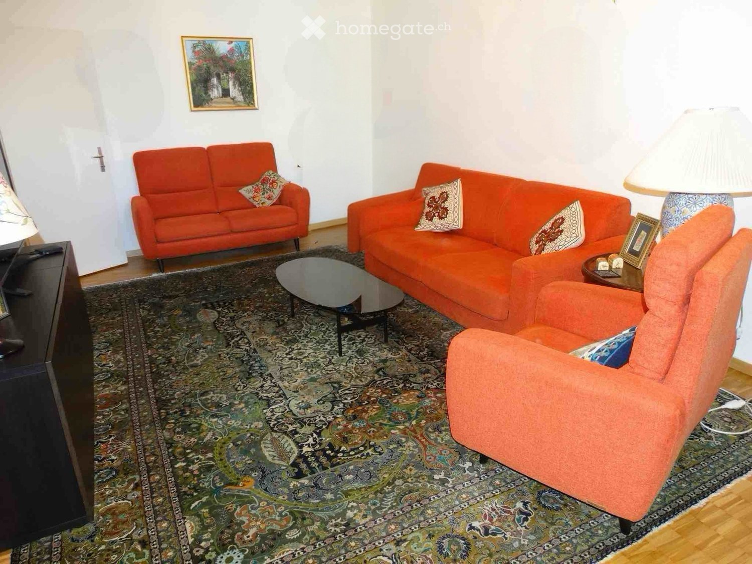 Living room with orange sofas, a patterned rug, a coffee table, a table lamp, and a picture frame on the wall.