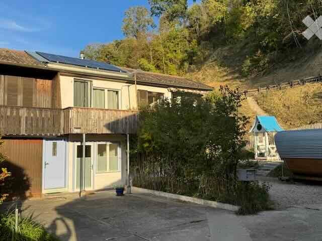 Two-story house with solar panels on the roof, wooden balcony, and surrounding greenery.