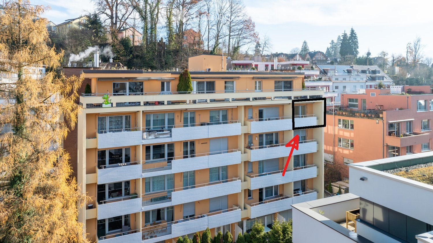 Multi-story residential building with balconies, large windows, and surrounding greenery.