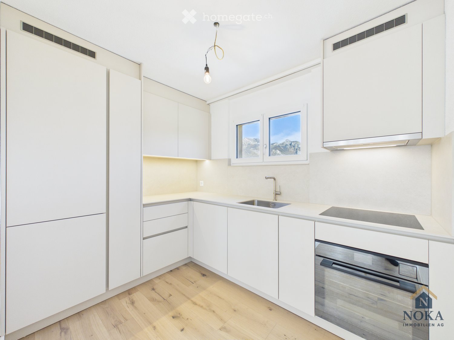 Modern kitchen with white cabinets, wooden flooring, and a window overlooking mountains.
