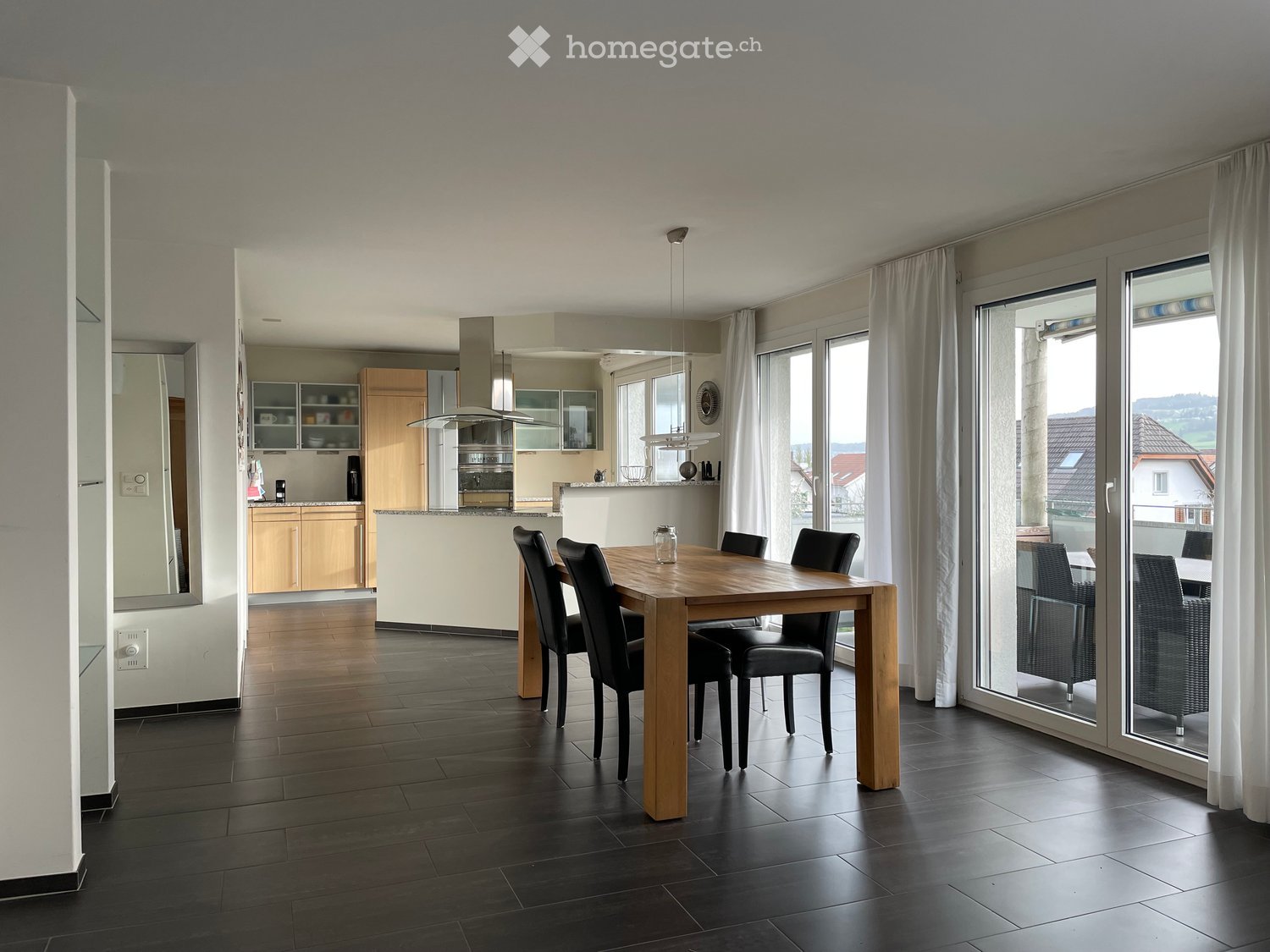 Modern dining area with a wooden dining table and black chairs, adjacent to a kitchen with light wood cabinets and stainless steel appliances.
