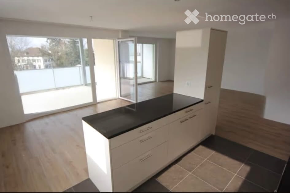 Empty kitchen with white cabinets, black countertop, and large windows overlooking a garden area.