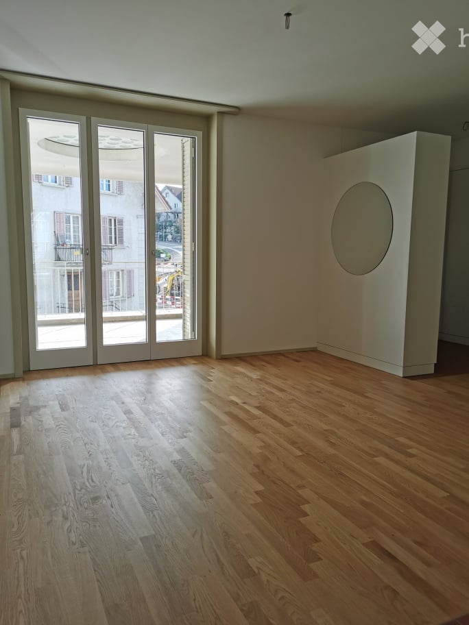 Empty room with wooden flooring, large glass sliding doors, and a white partition with a circular cutout.
